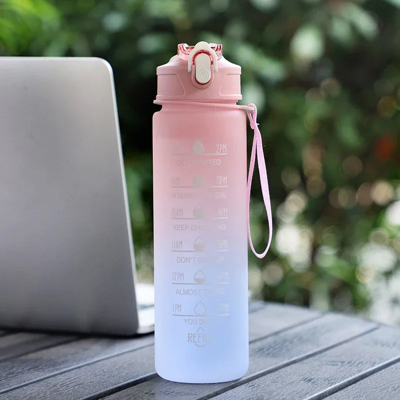 Gradient pink to white water bottle with motivational quotes on a wooden surface with a laptop in the background.